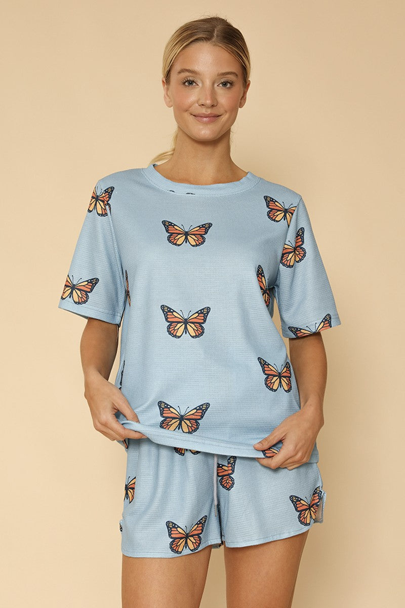 Woman wearing a light blue pajama set with monarch butterfly patterns on a beige background