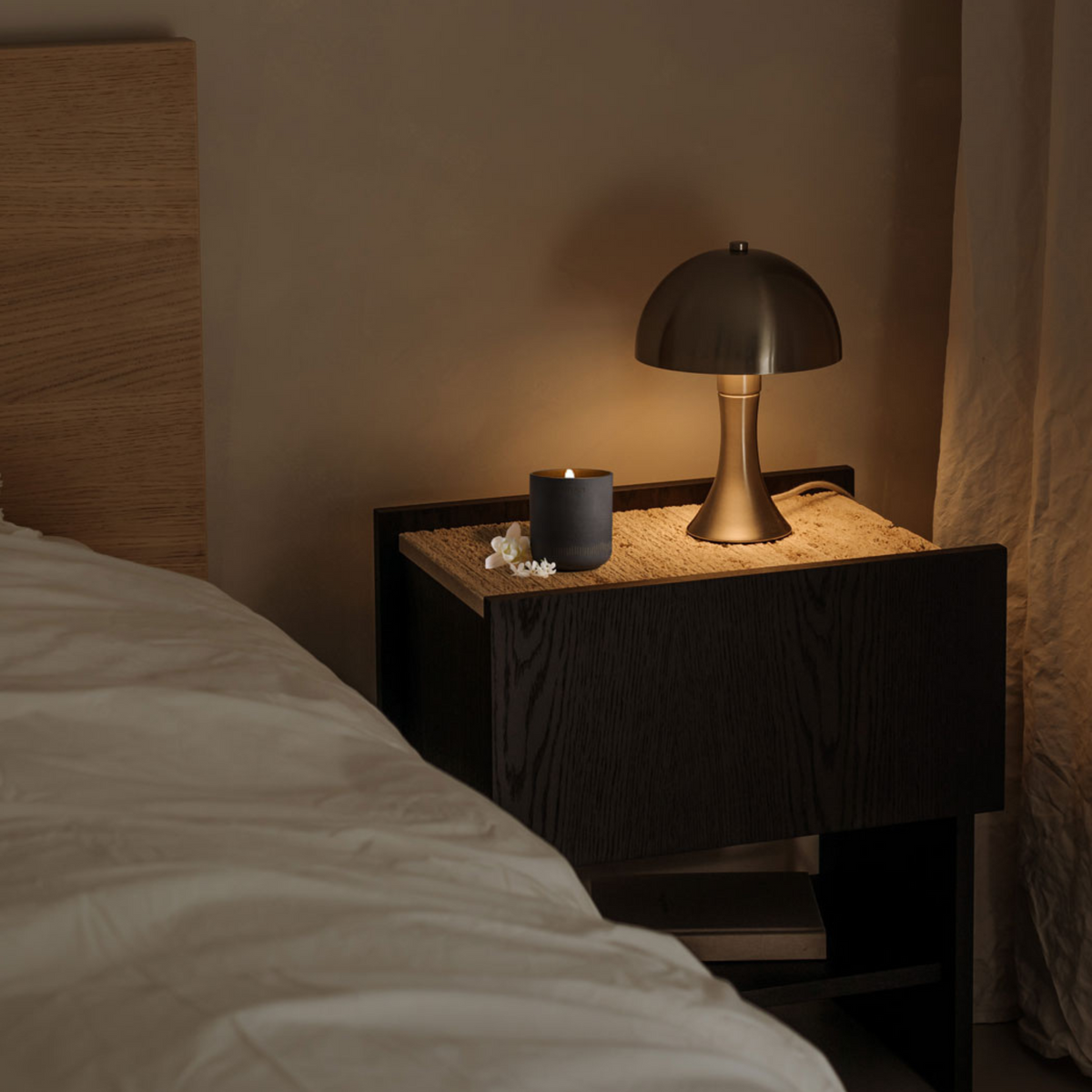 Nighstand with a lamp and candle next to a bed in a dimly lit room