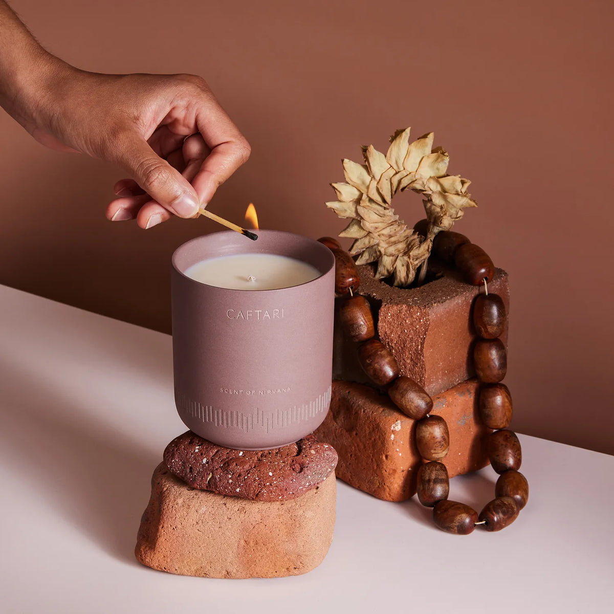 Hand lighting a candle labeled 'CAFtAri' with decorative elements on a neutral background