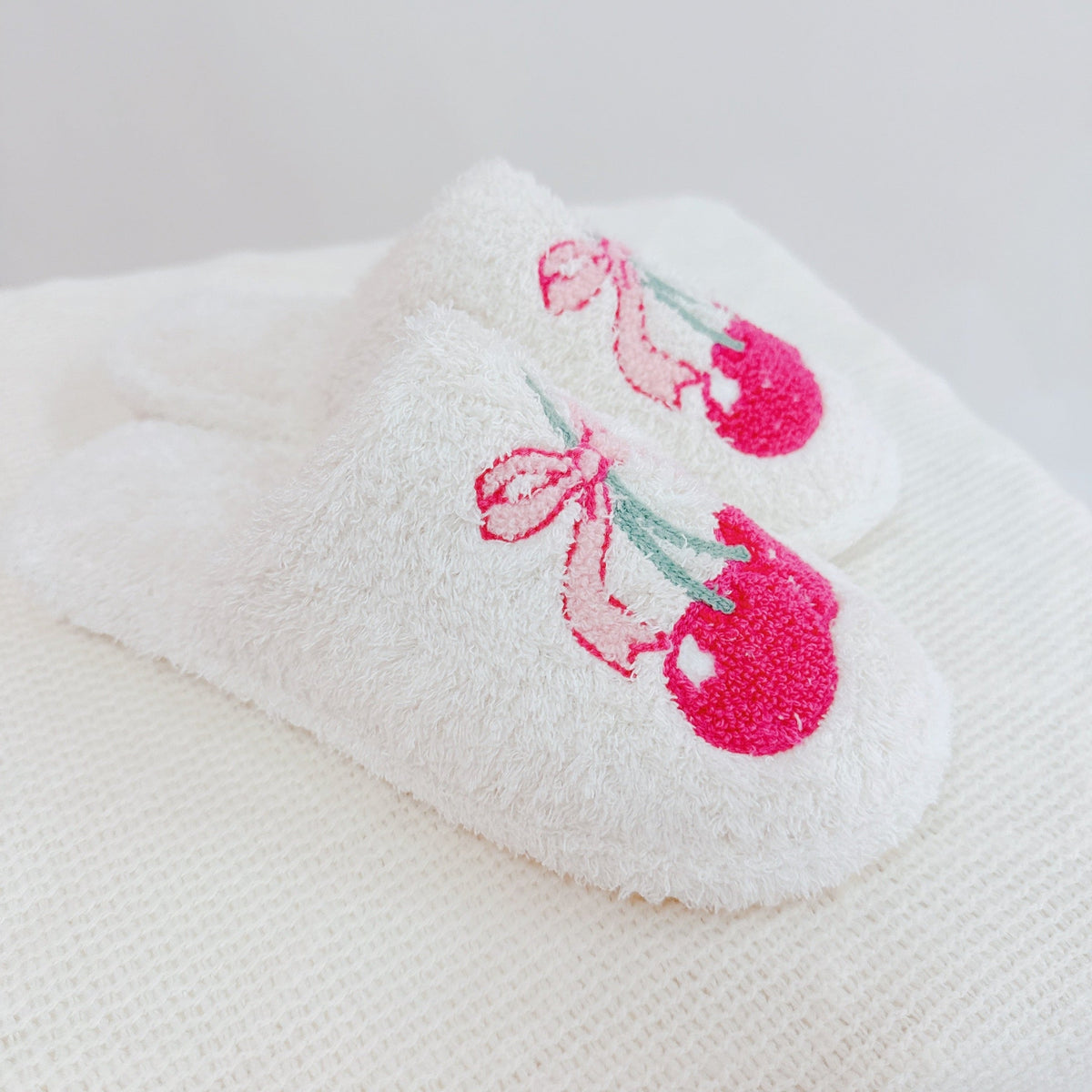 White slippers with pink embroidered design on a white background