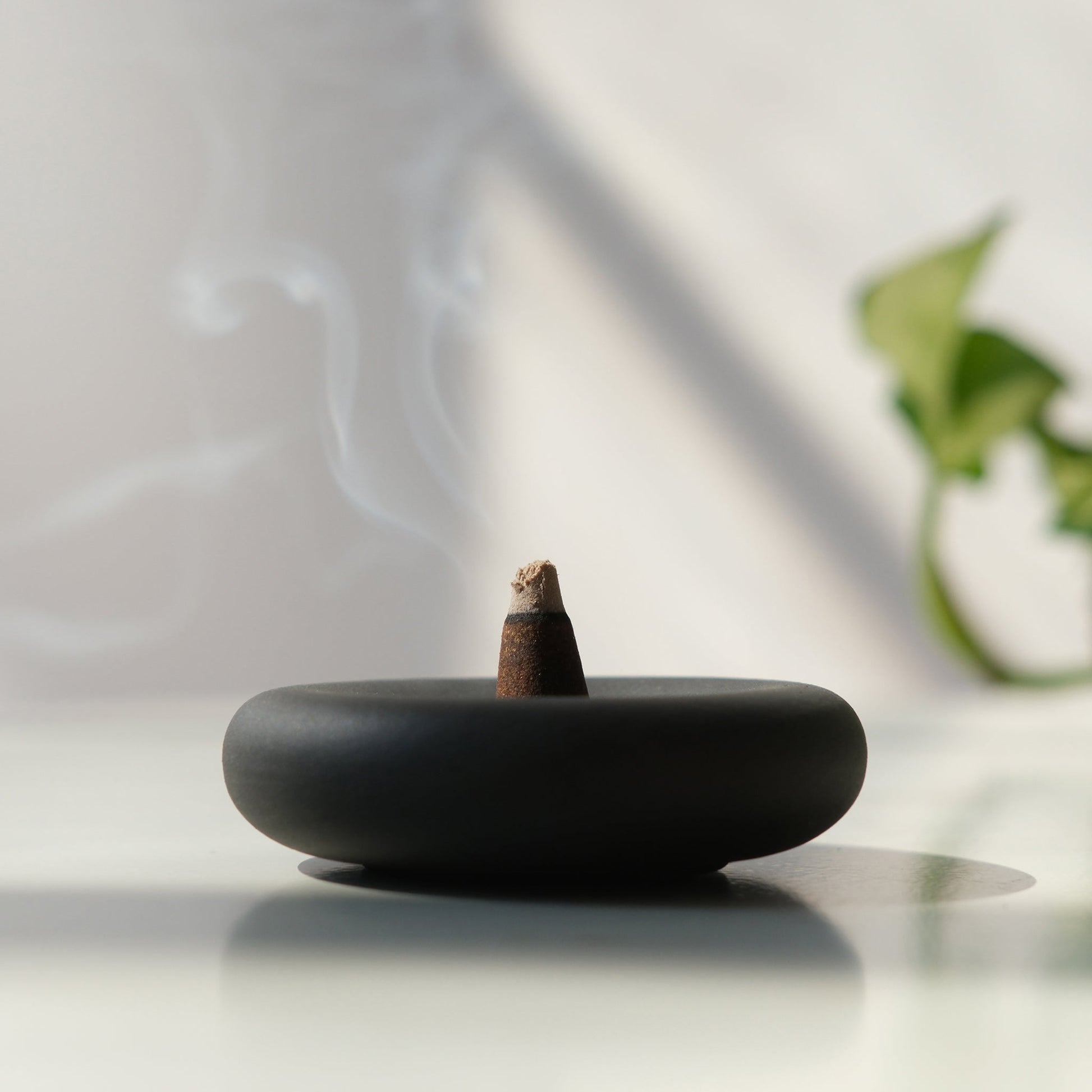 handmade Black incense burner with a smoking incense stick on a light surface.