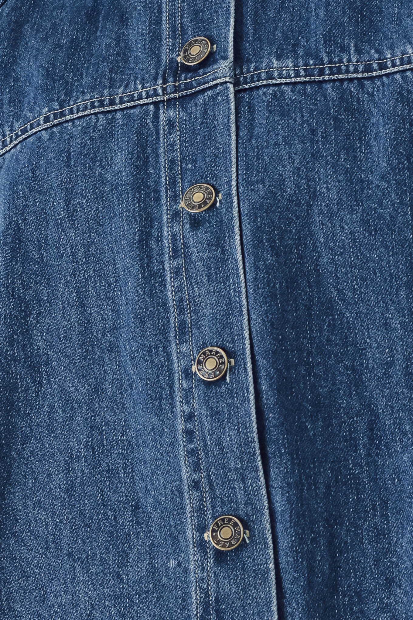 Close-up of a blue denim button-front garment, showing the denim fabric texture and a vertical row of round metal buttons.