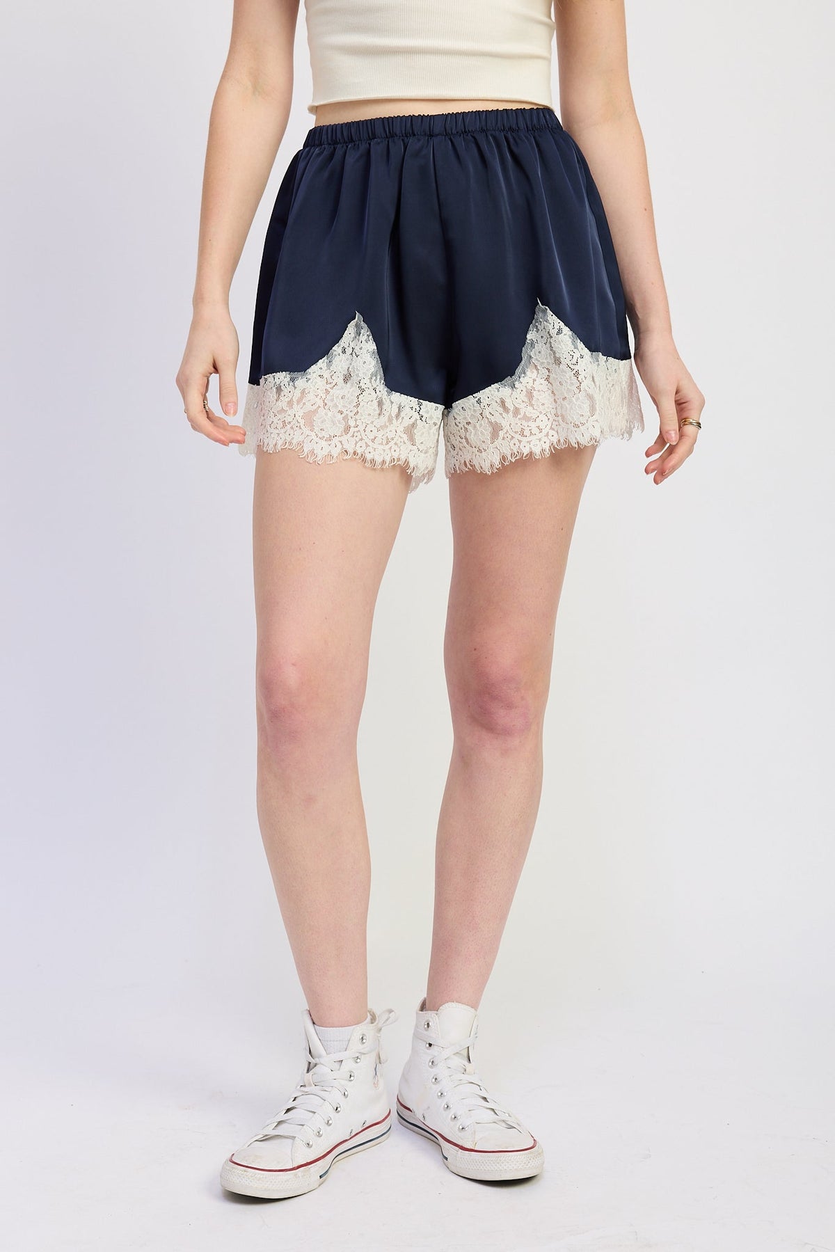 Person wearing navy shorts with lace trim and white high-top sneakers on a plain background