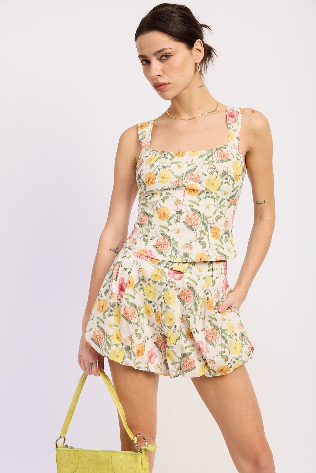 Woman wearing a floral dress holding a yellow handbag against a white background