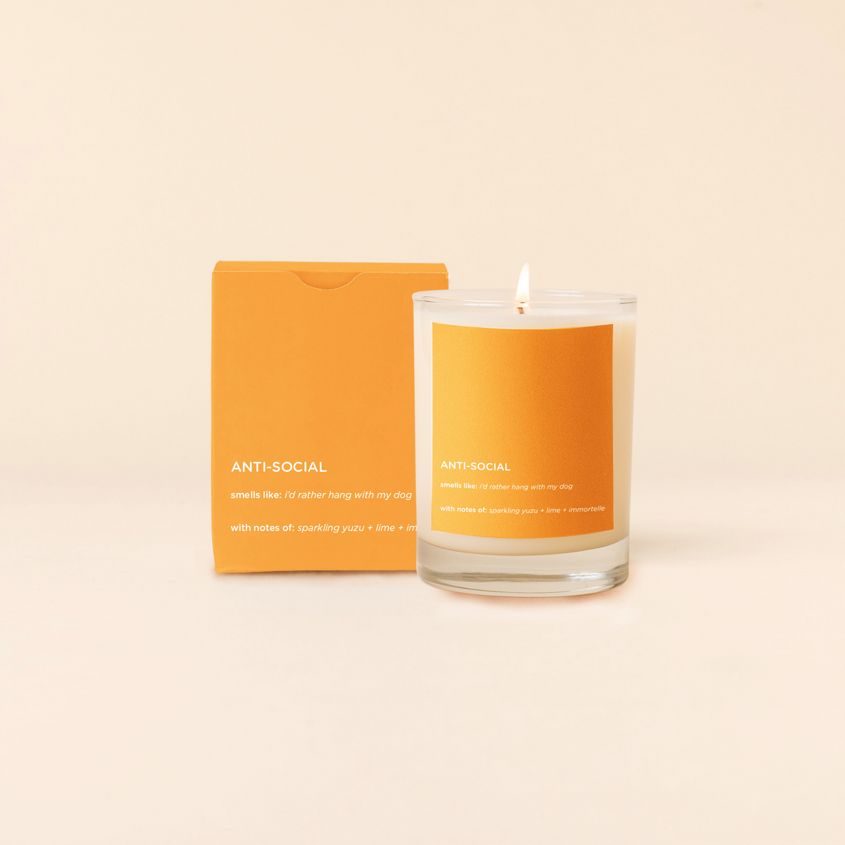 Anti-social Candle with orange label and packaging on a beige background