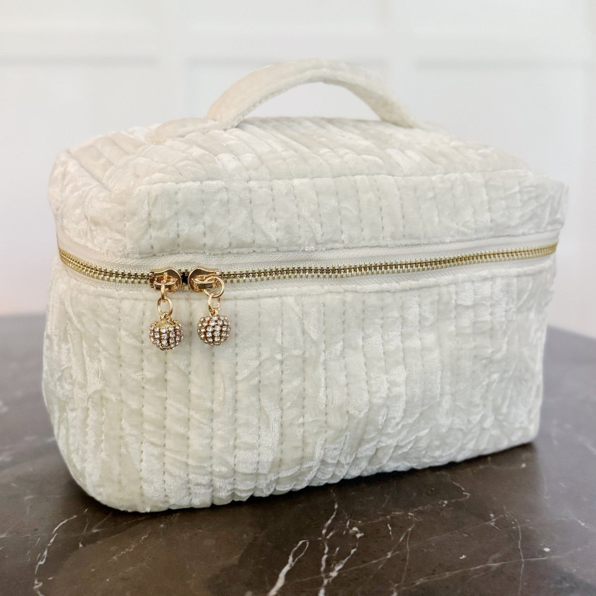 White textured makeup bag with gold zipper on a marble surface