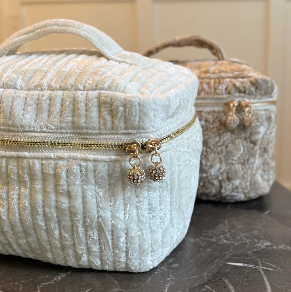Two cream-colored textured makeup bags with gold zippers on a dark surface.