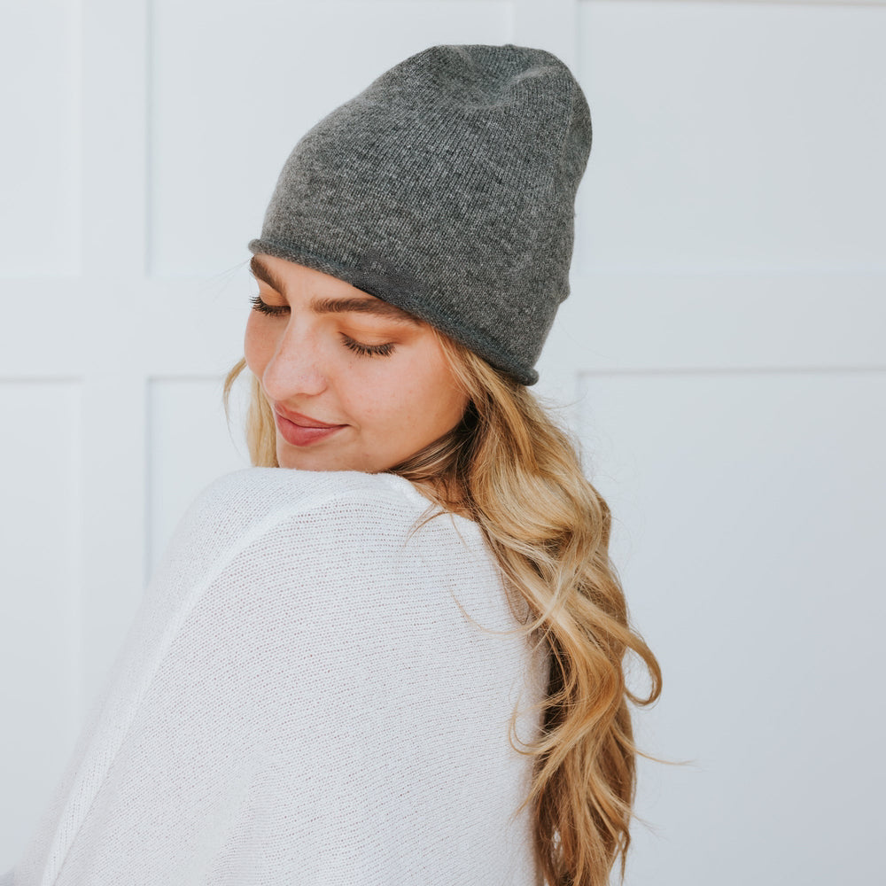 Woman wearing a gray knit beanie and white sweater against a light background