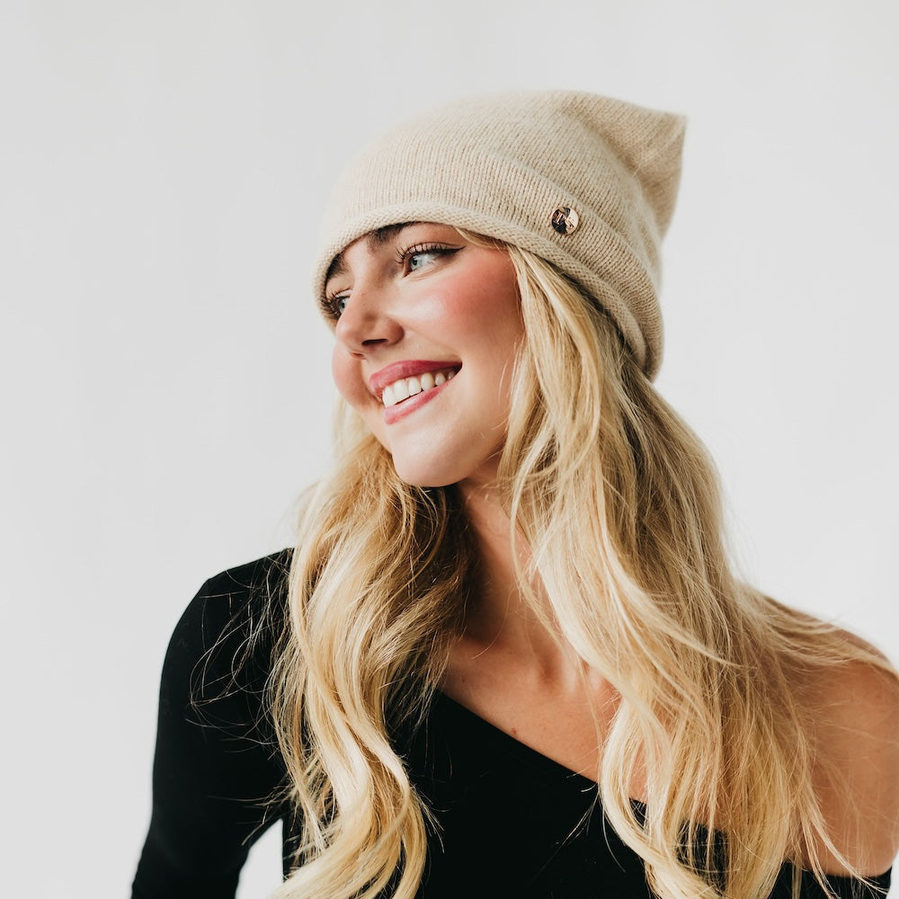 Woman wearing a beige beanie and black top against a white background
