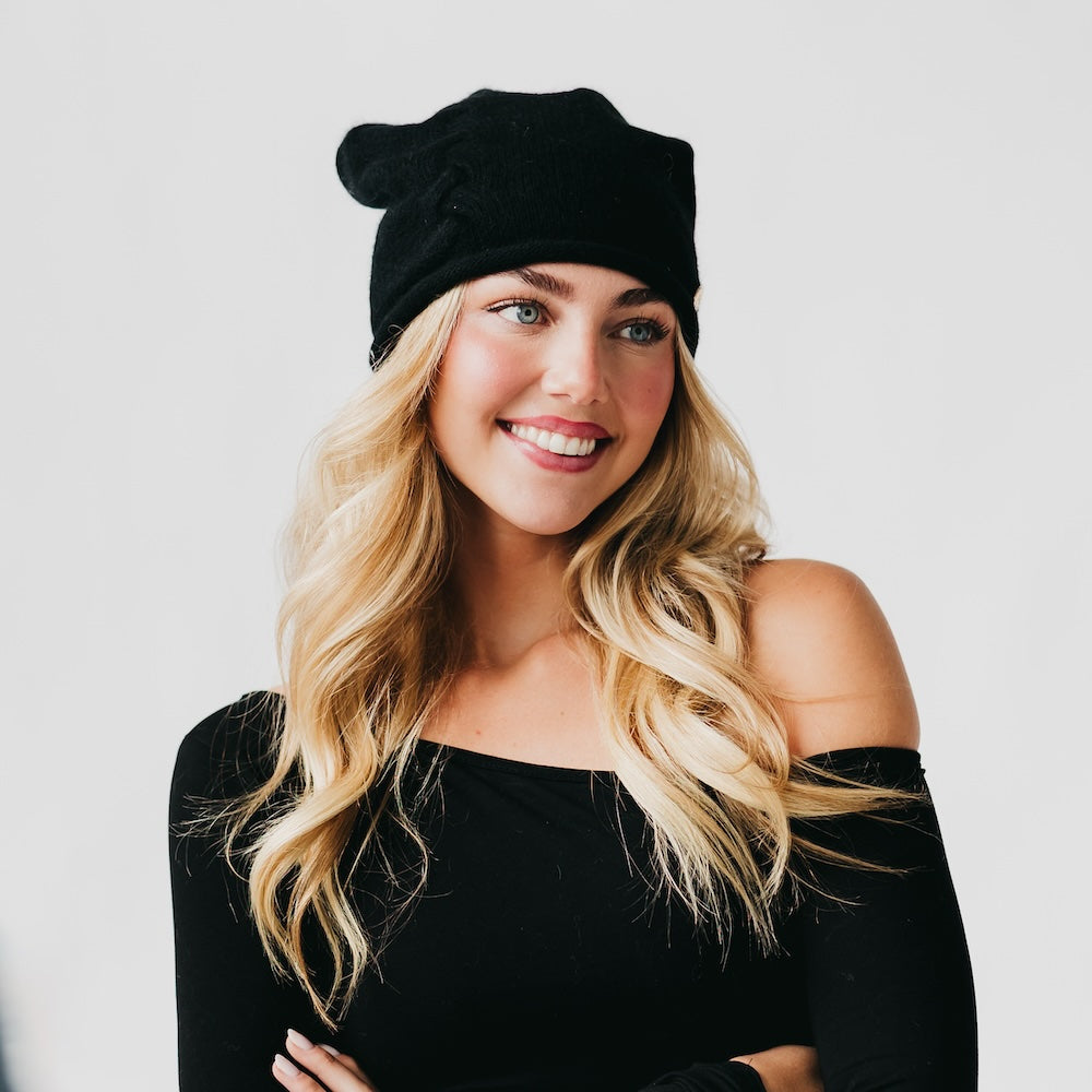 Woman wearing a black beanie and black top against a light gray background