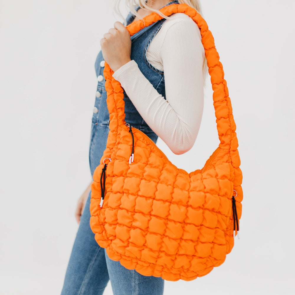 Person holding an orange quilted handbag against a white background