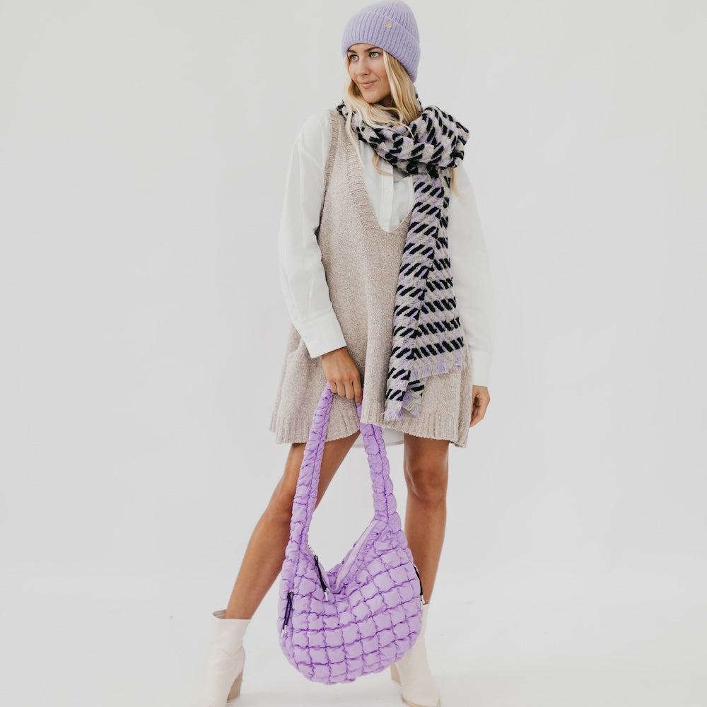 Woman wearing a purple knit hat and bag, holding a patterned scarf against a white background