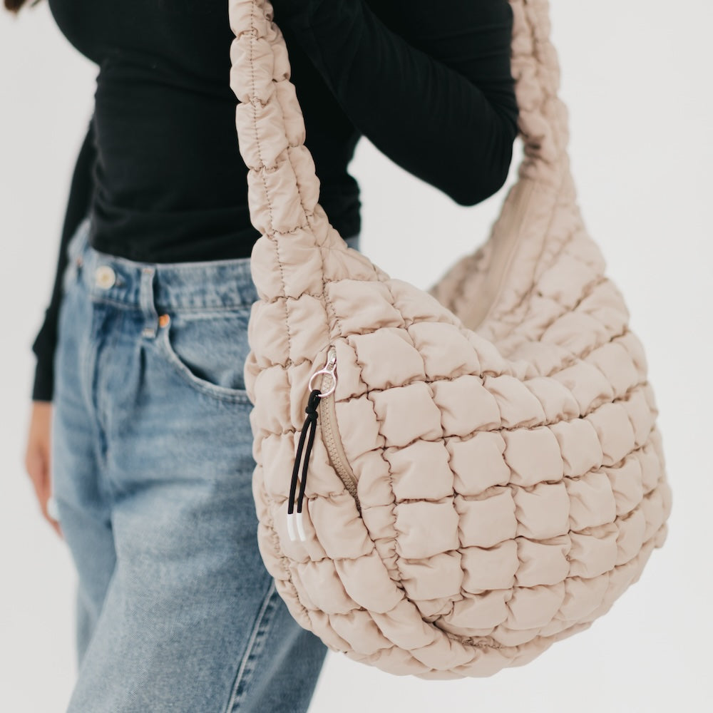 Beige woven handbag held by a person wearing a black top and blue jeans on a white background