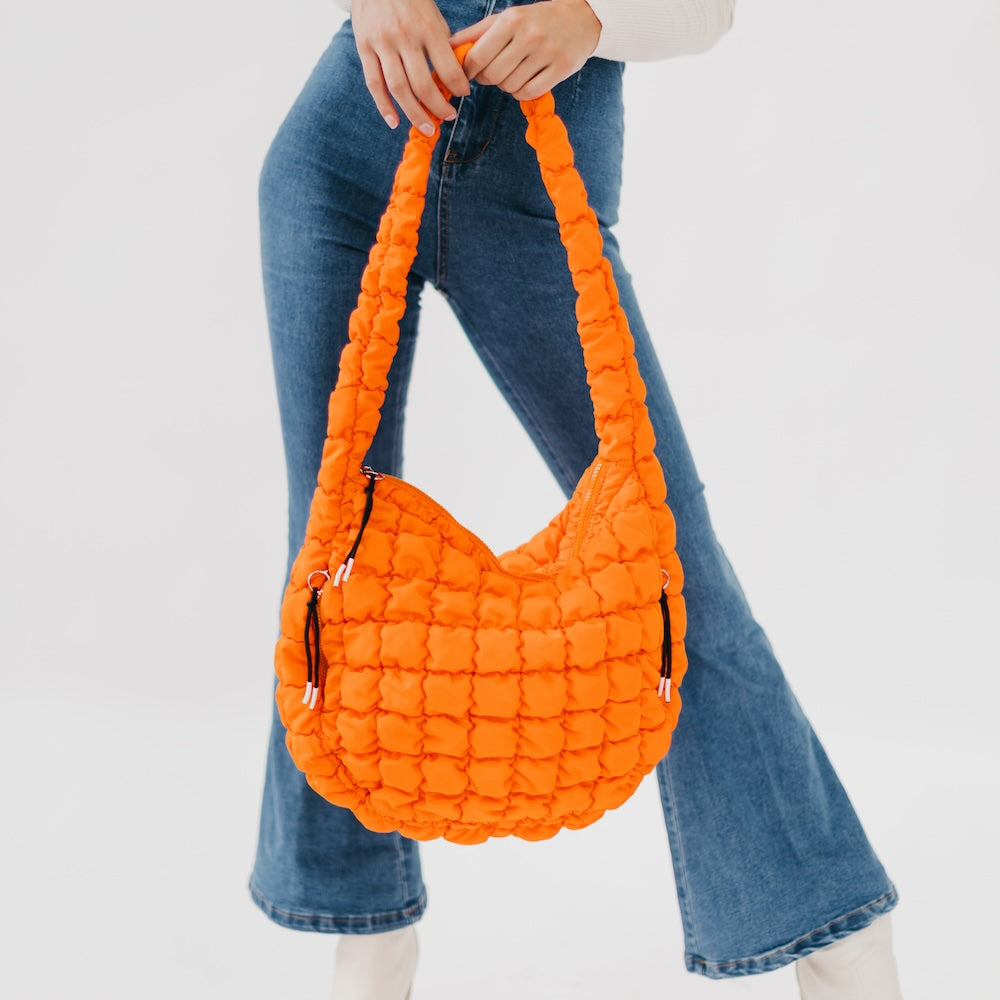 Person holding an orange quilted handbag against a plain background