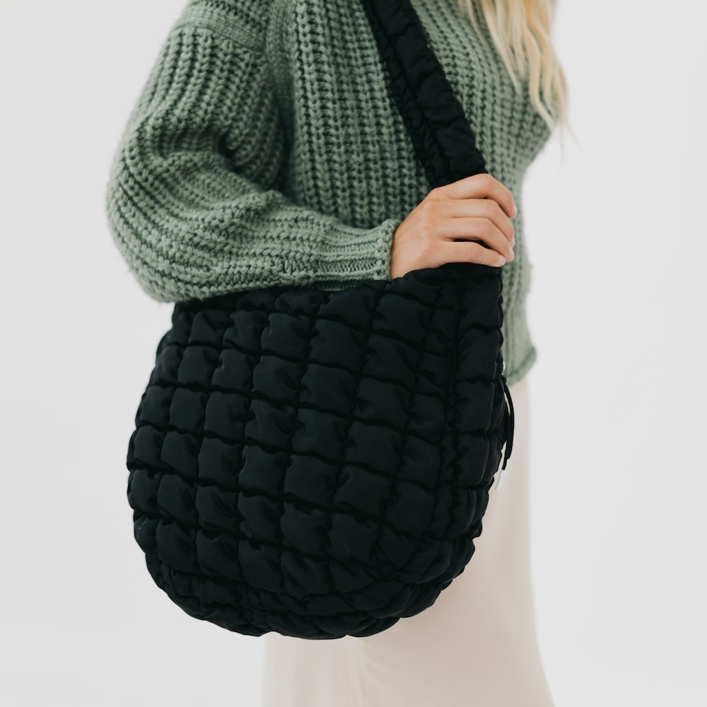 Person wearing a green knitted sweater holding a black woven bag against a white background
