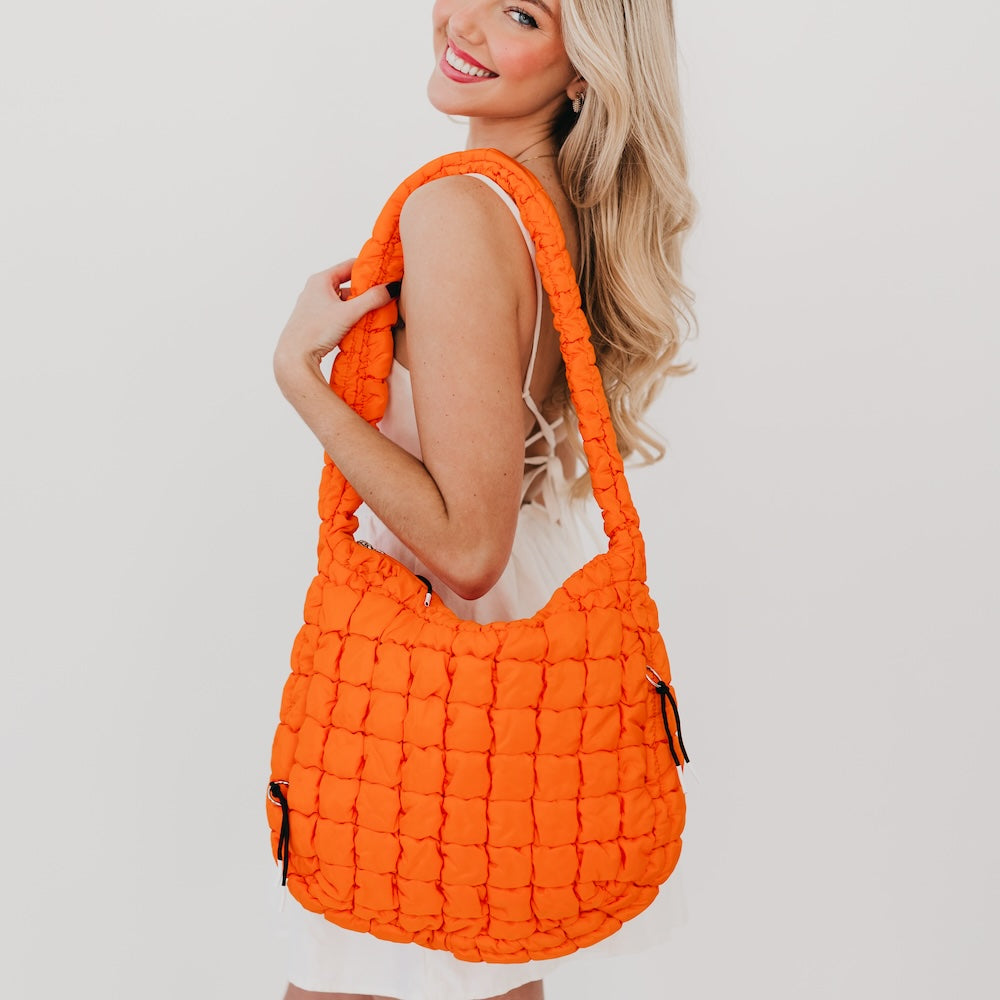 Woman holding an orange quilted handbag against a plain background
