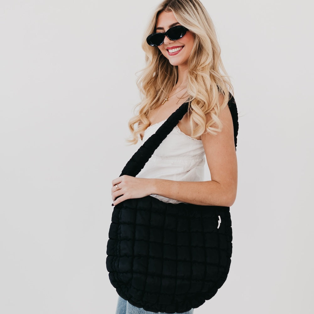 Woman holding a black quilted bag against a plain background