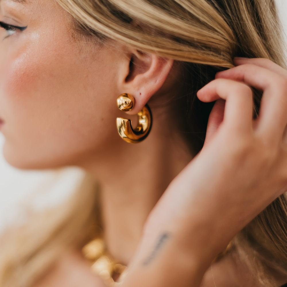 Close-up of a woman wearing gold hoop earrings with a blurred background