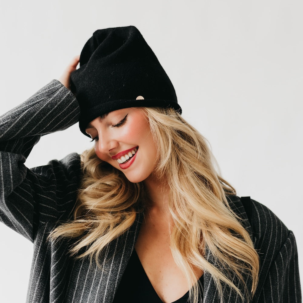 Woman wearing a black beanie and gray pinstripe coat against a white background