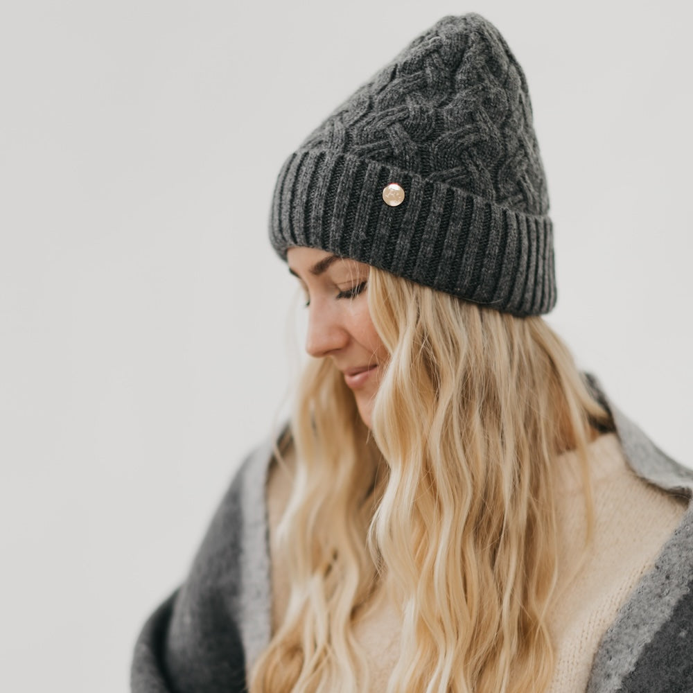 Woman wearing a gray knit beanie with satin lined interior with a gold button on a light gray background