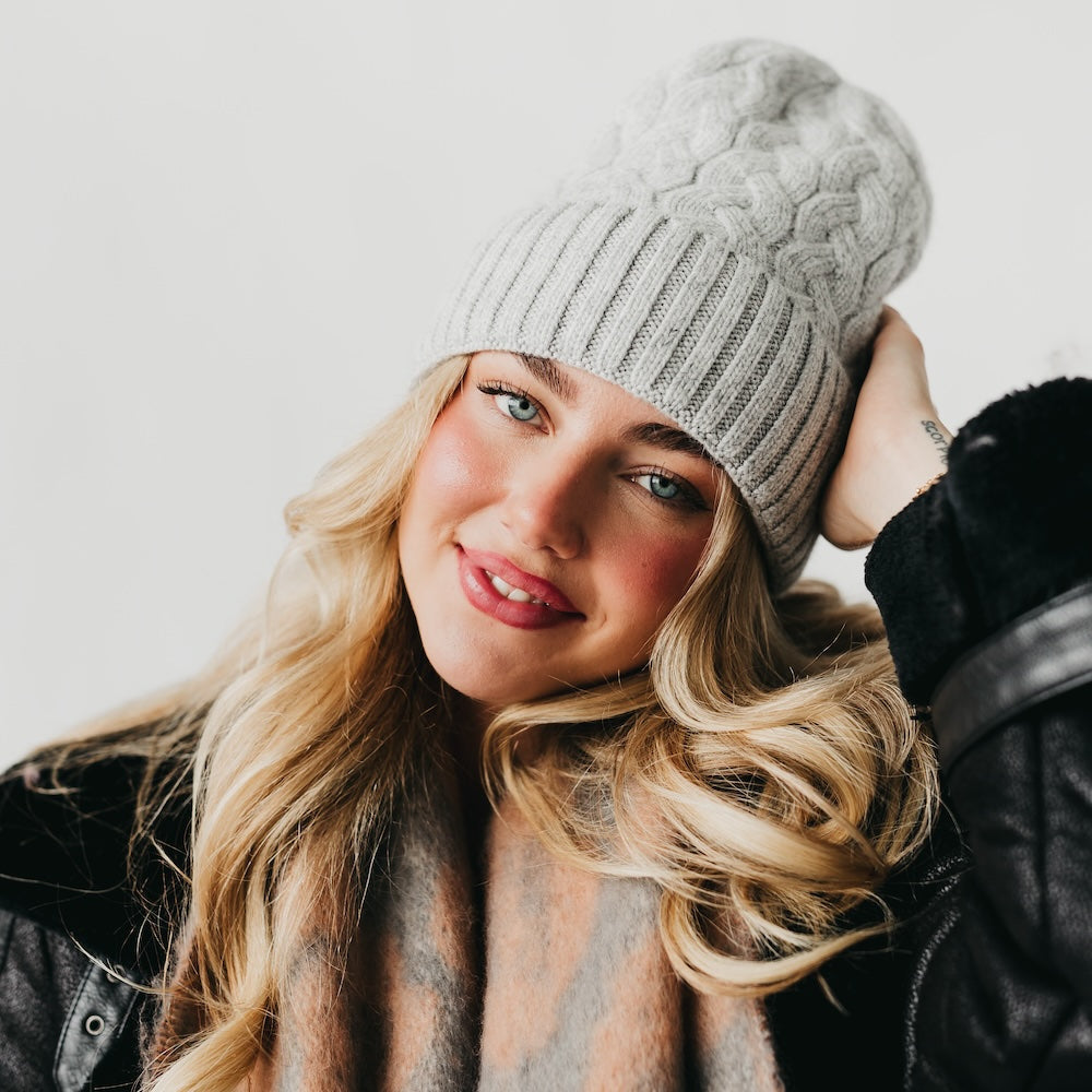 Woman wearing a gray knit beanie with satin lined interior and black leather jacket against a white background