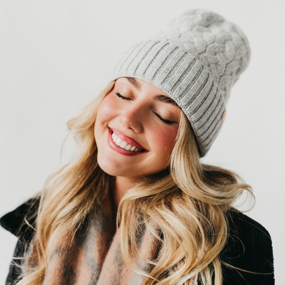 Woman wearing a gray knit beanie with satin lined interior and plaid scarf against a white background