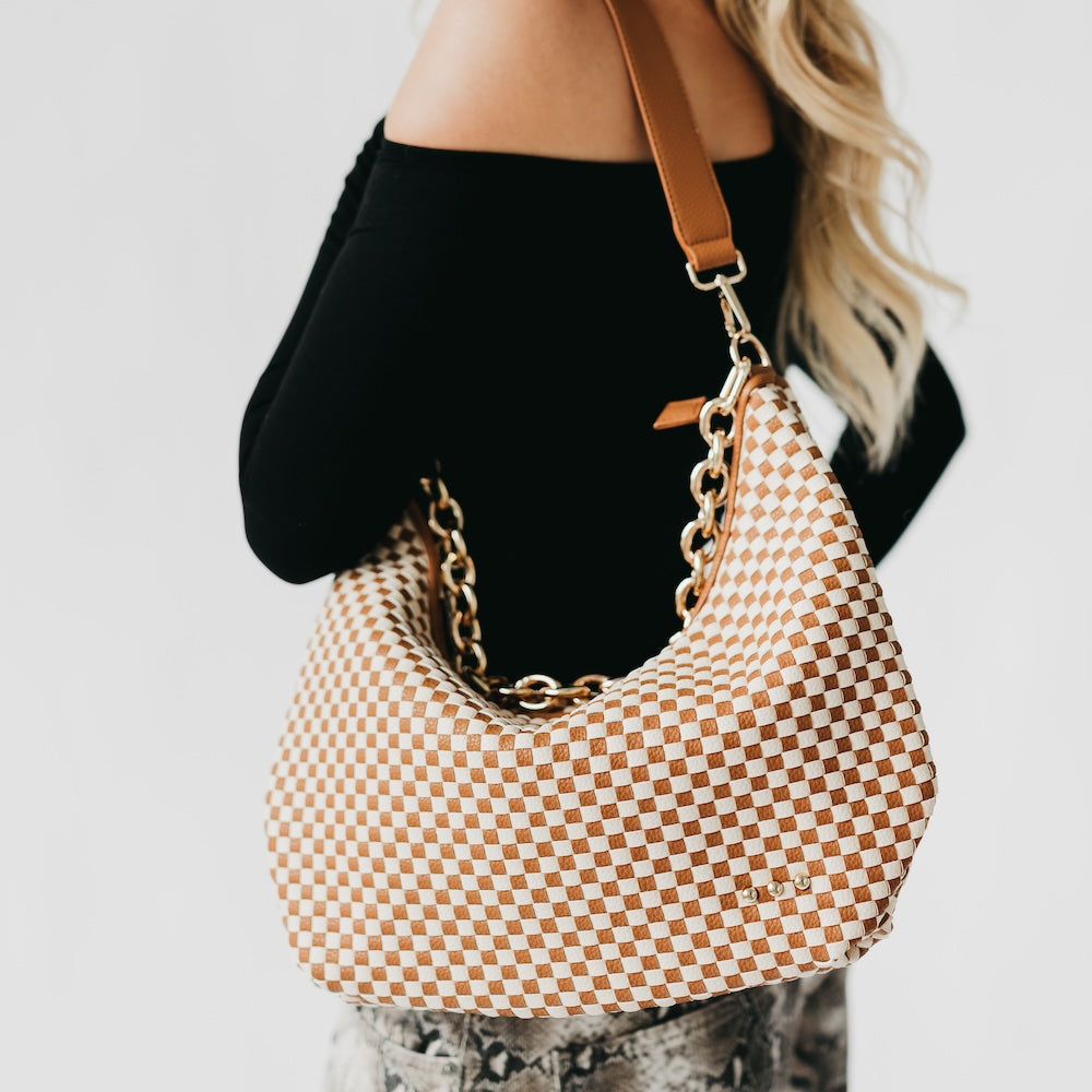 Person holding a checkered handbag with a gold chain strap against a neutral background