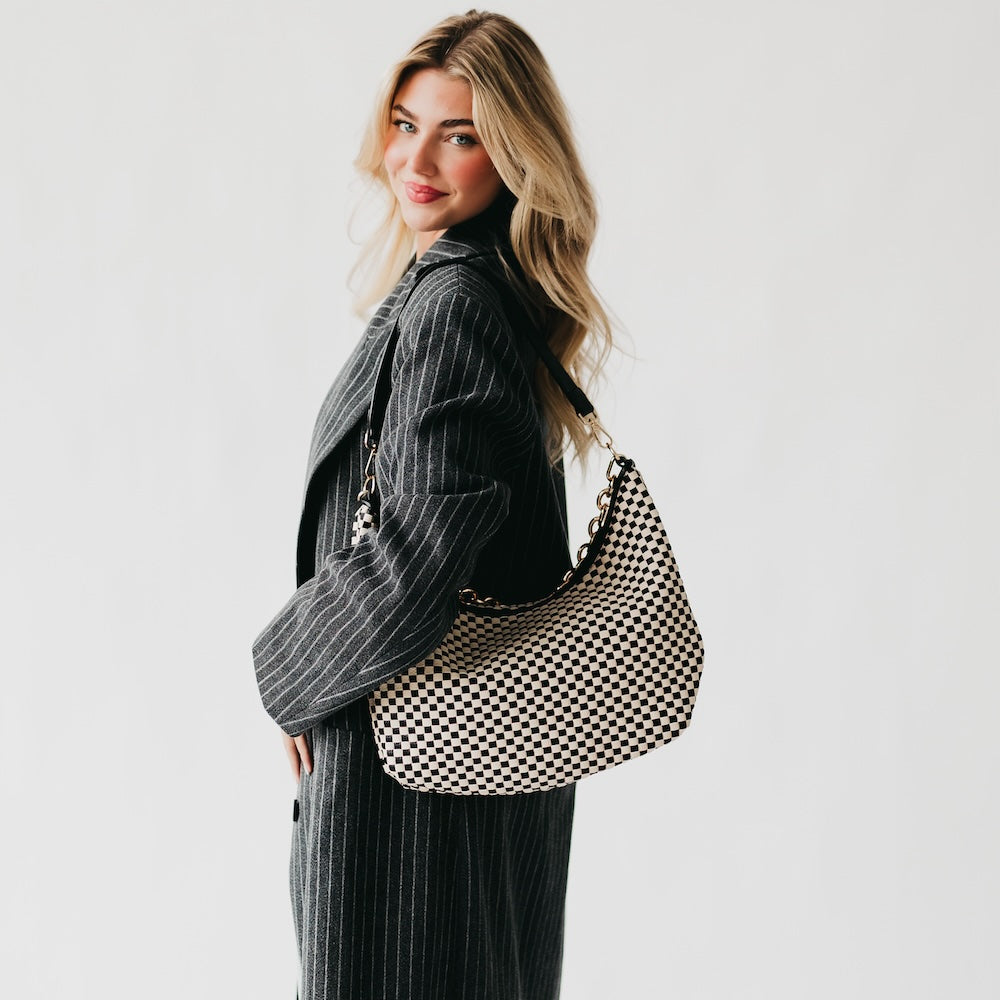 Woman holding a black and white checkered bag against a plain background