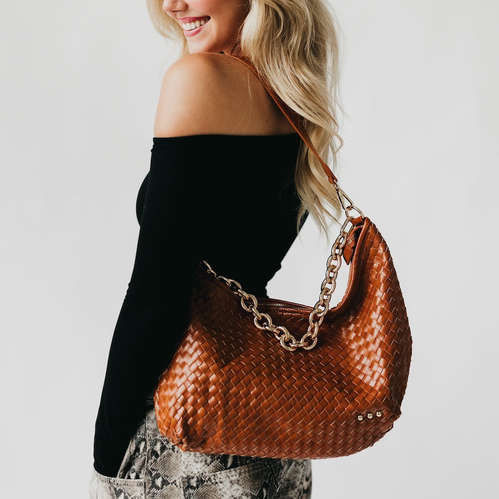 Woman holding a brown woven handbag with a gold chain strap on a plain background