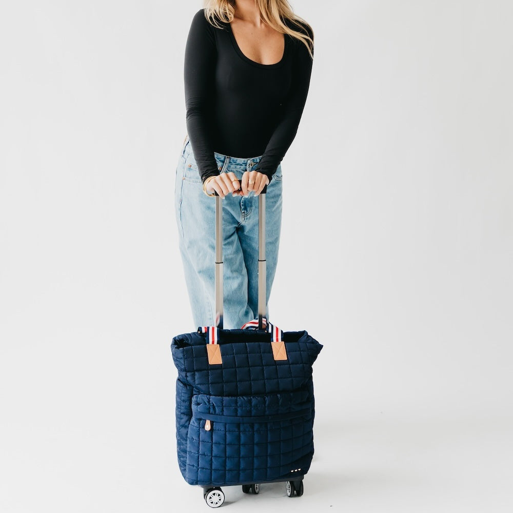 Person holding a navy quilted suitcase on a light gray background