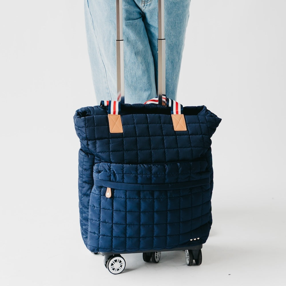 Blue quilted rolling bag with a person wearing jeans on a white background