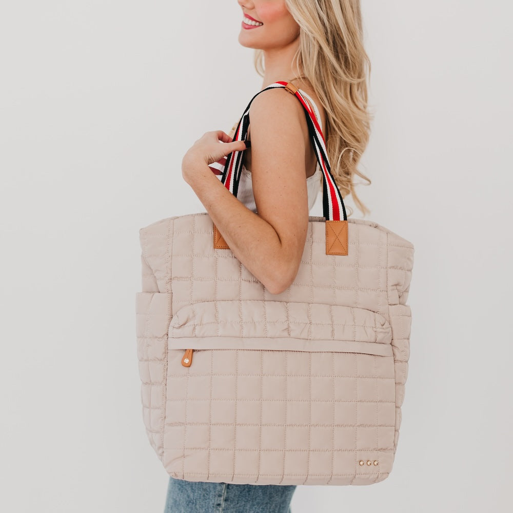 Woman holding a beige quilted tote bag with a white background