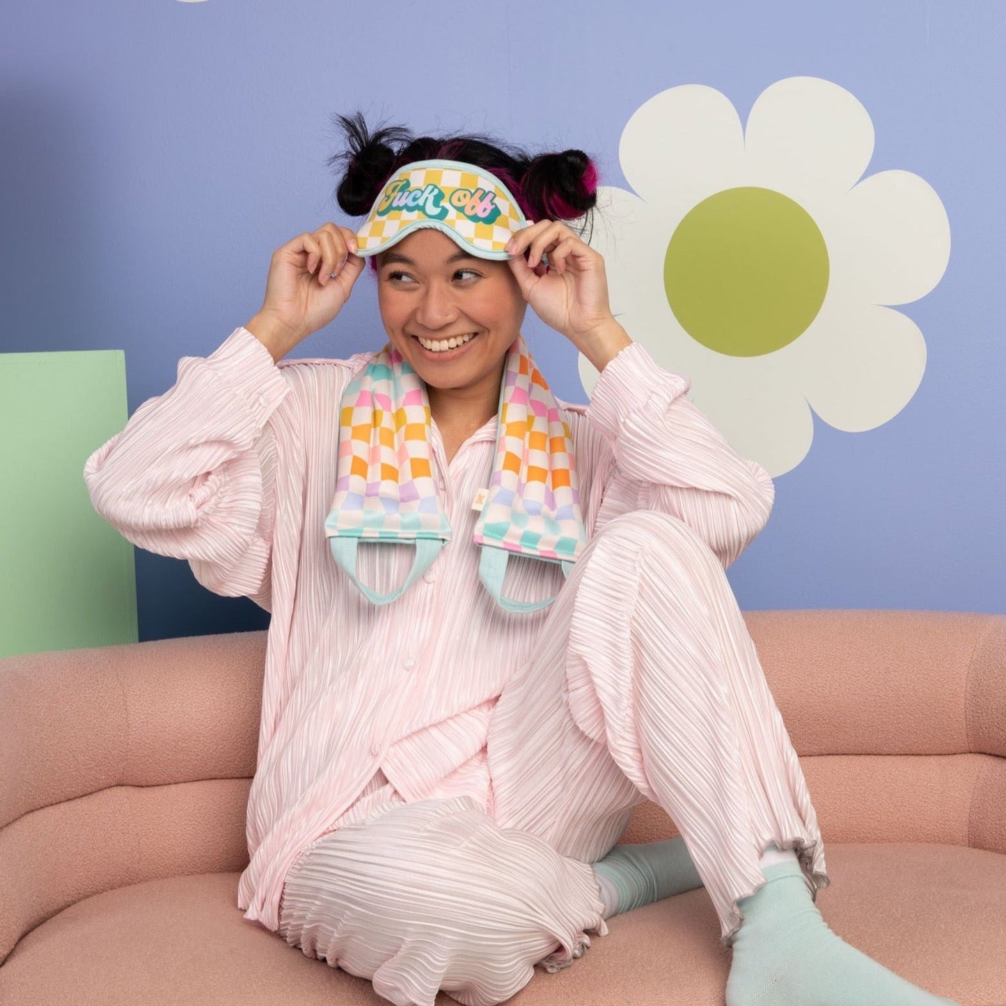 Person wearing a colorful eye mask and scarf, sitting on a couch with a playful background.