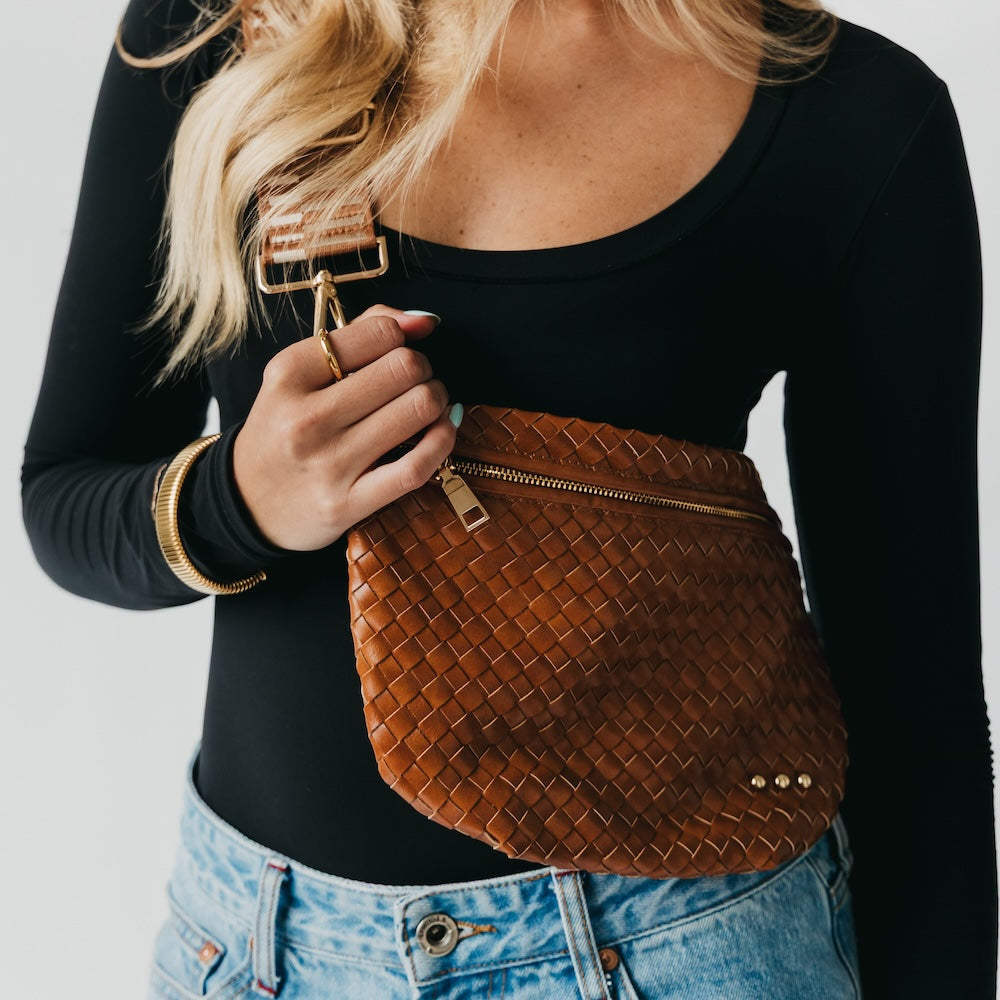 Person holding a brown woven handbag against a neutral background