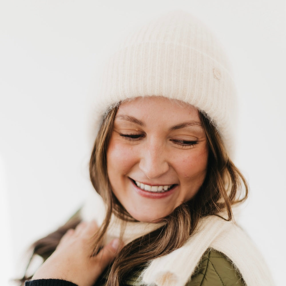 Woman wearing a white knit hat and scarf against a light background