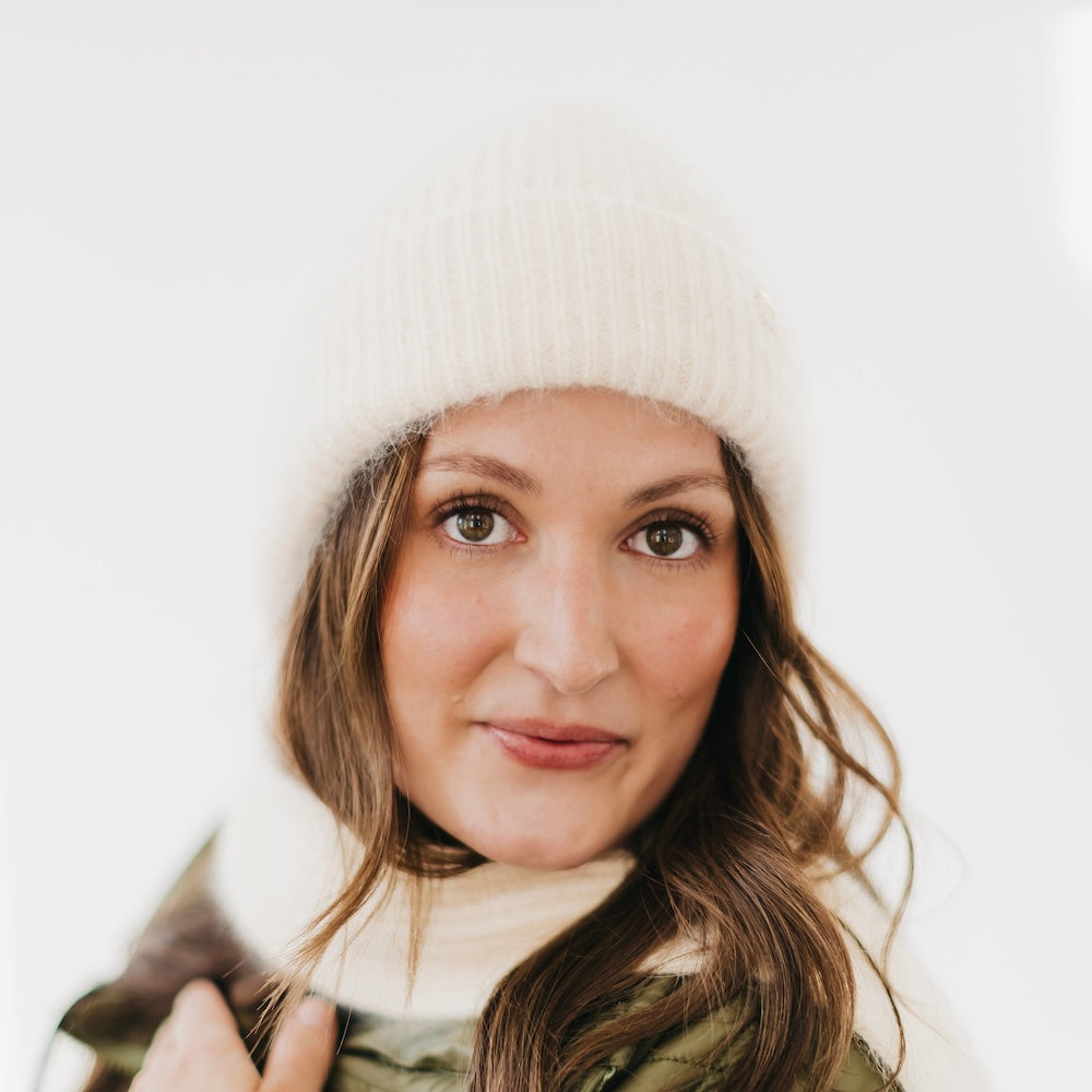 Woman wearing a white knit hat and scarf against a light background