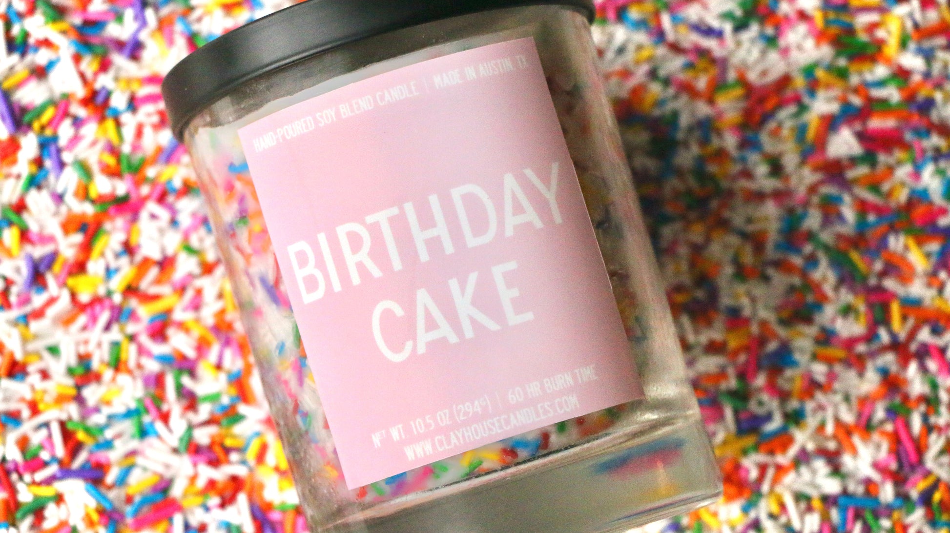 Candle jar labeled 'Birthday Cake' on a background of colorful sprinkles
