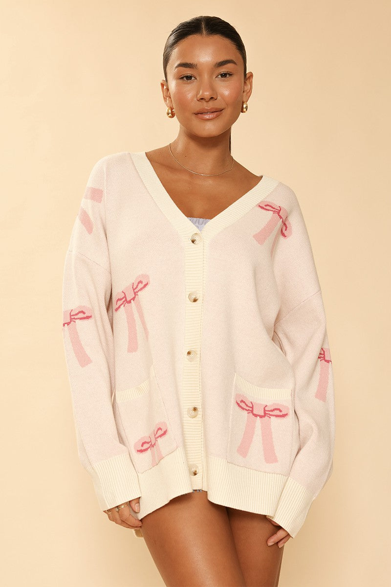Woman wearing a cream cardigan with pink bows on a beige background