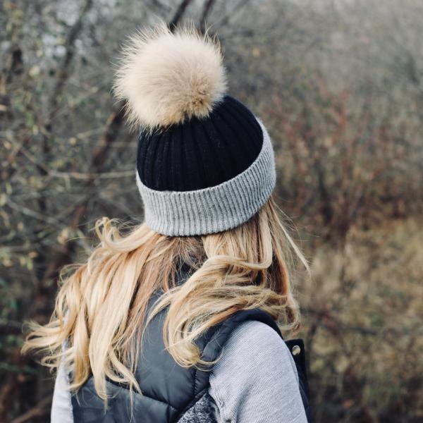 Person wearing a black and gray knit beanie with a pom-pom in a natural setting.