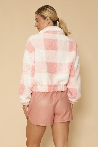 Woman wearing a pink and white checkered fleece jacket and pink shorts on a beige background