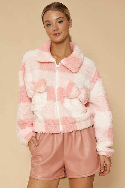 Woman wearing a pink and white checkered fleece jacket and shorts on a beige background