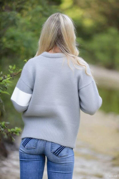 Person wearing a gray sweater and blue jeans walking outdoors with a blurred natural background
