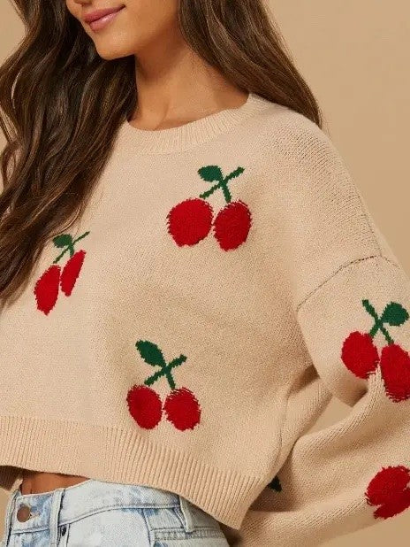 Beige sweater with cherry designs worn by a person