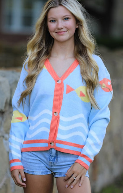 Woman wearing a colorful cardigan with a light blue background fish patterns outdoors 