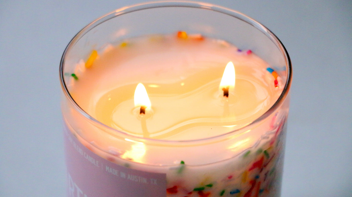 Candle with colorful sprinkles in a glass container on a light blue background