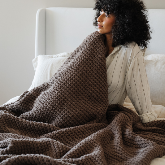 Woman wrapped in a brown WAFFLE KNIT XL THROW BLANKET sitting on a couch.