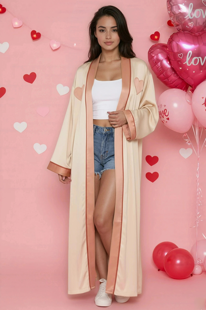 Woman in a long beige coat standing in front of a pink background with heart shapes and balloons.