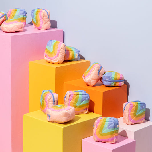 Colorful rainbow-patterned pouches on geometric pink, orange, and yellow blocks against a light blue background.