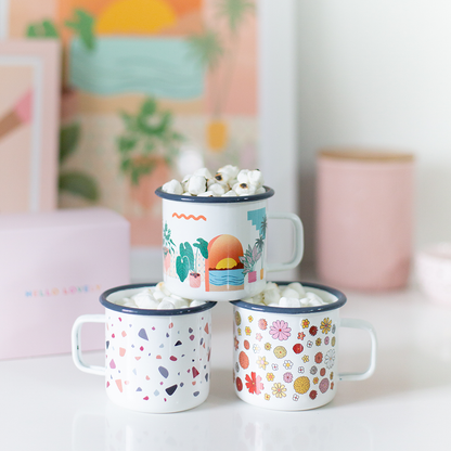 Three campfire mugs with colorful designs on a white surface, one filled with popcorn.