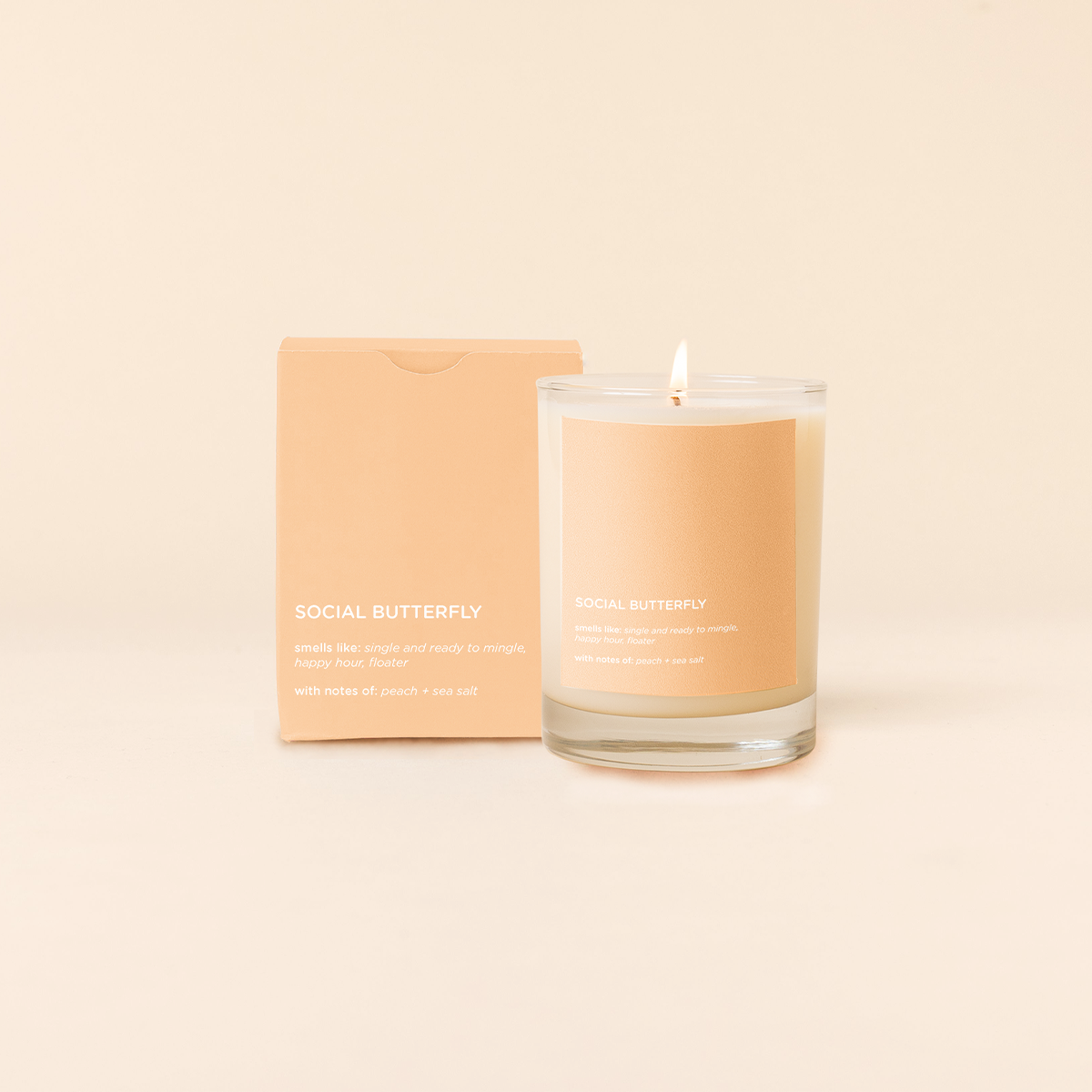Candle labeled 'Social Butterfly' with packaging on a beige background